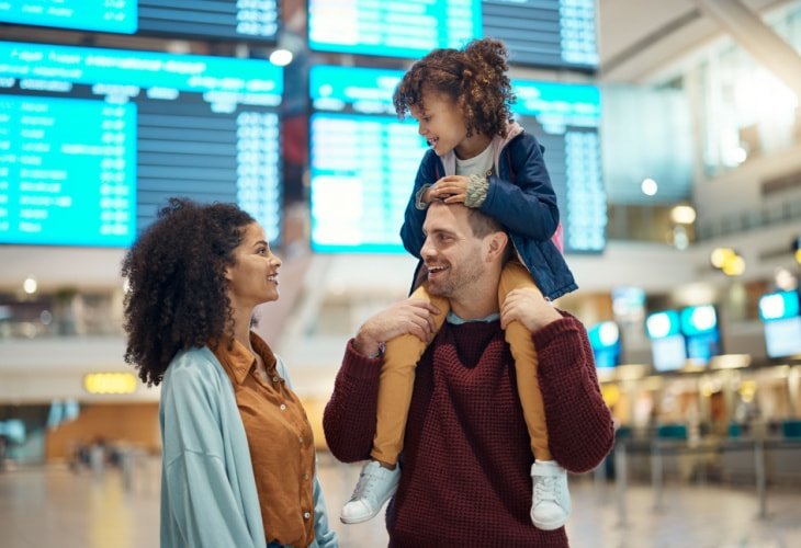 Smiling family in airport with child sitting on one parent's shoulders